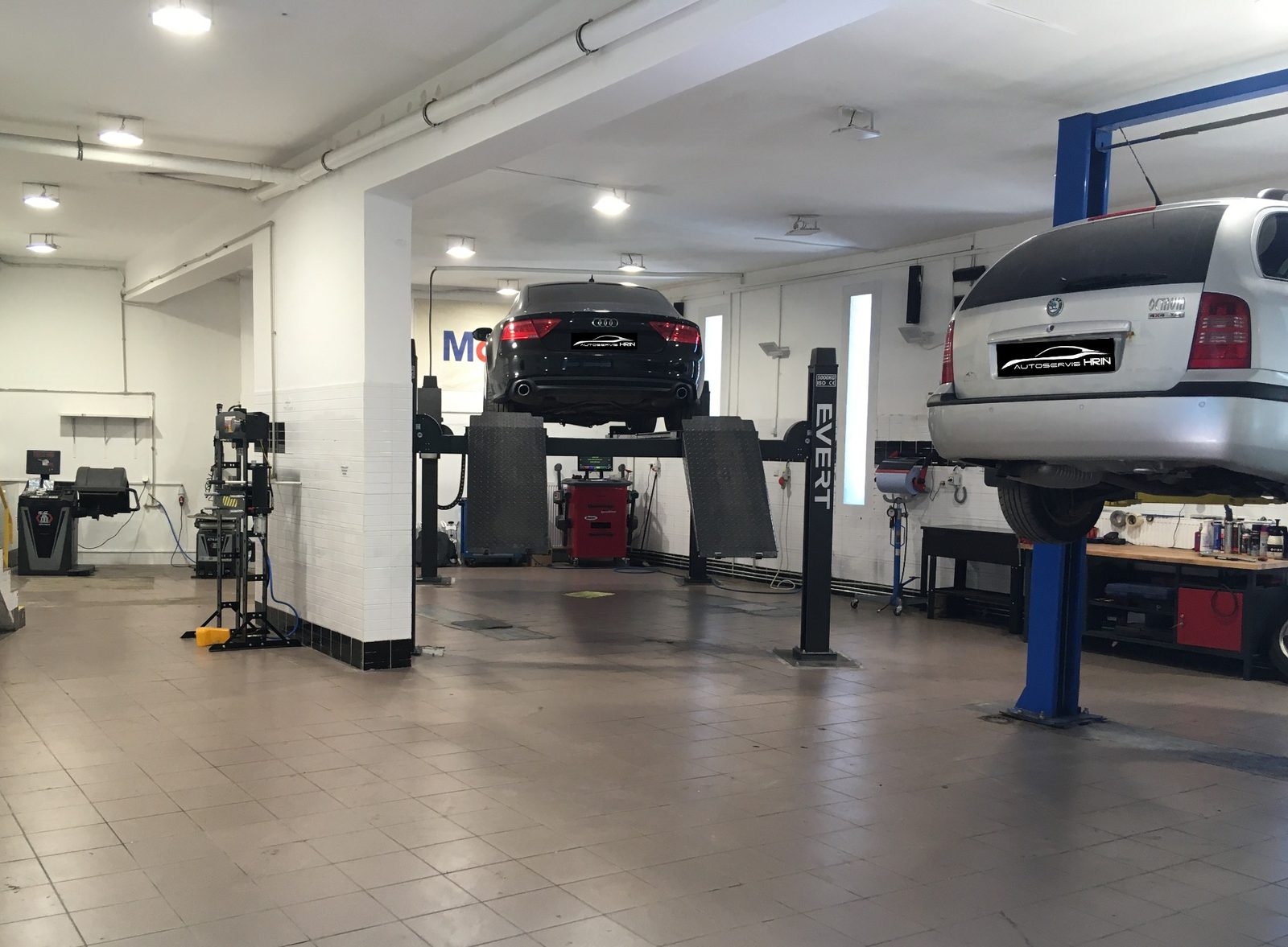 Hala dielne Autoservisu Hriň: dve autá na zdvihákoch, biely obklad